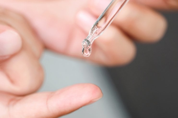 Ein Tropfen eines Hyaluronsäure-Serums tropft aus einer Pipette auf einen Finger